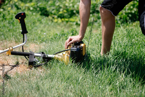 Gardener mows the grass with a trimmer in the yard in the summer.