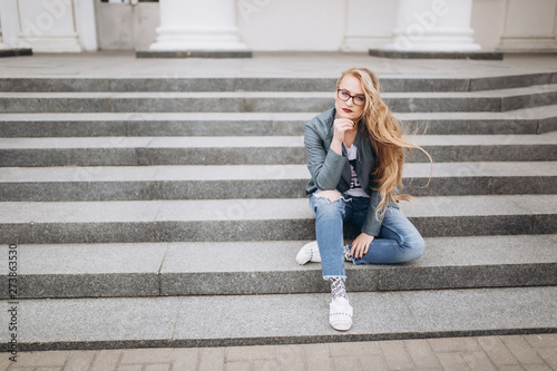 Young caucasian blondie hipster woman with long curly hairstyle in eye glasses in the city street. Freelance, freedom, beauty, happy lifestyle concept