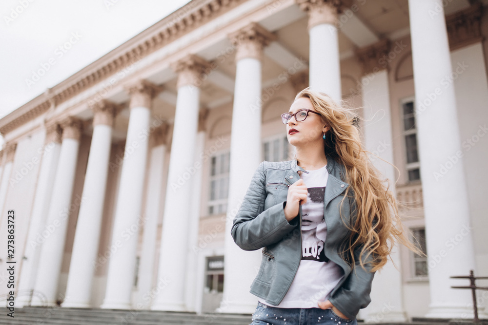Fototapeta premium Young caucasian blondie hipster woman with long curly hairstyle in eye glasses in the city street. Freelance, freedom, beauty, happy lifestyle concept