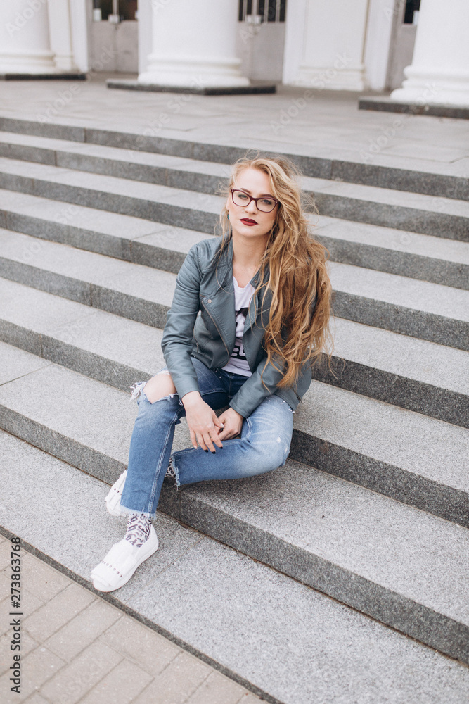 Young caucasian blondie hipster woman with long curly hairstyle in eye glasses in the city street. Freelance, freedom, beauty, happy lifestyle concept