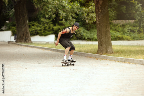 Skateboarder doing a trick at the city's street in cloudly day. Young man in sneakers and cap riding and longboarding on the asphalt. Concept of leisure activity, sport, extreme, hobby and motion.