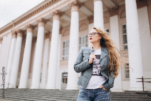 Young caucasian blondie hipster woman with long curly hairstyle in eye glasses in the city street. Freelance, freedom, beauty, happy lifestyle concept