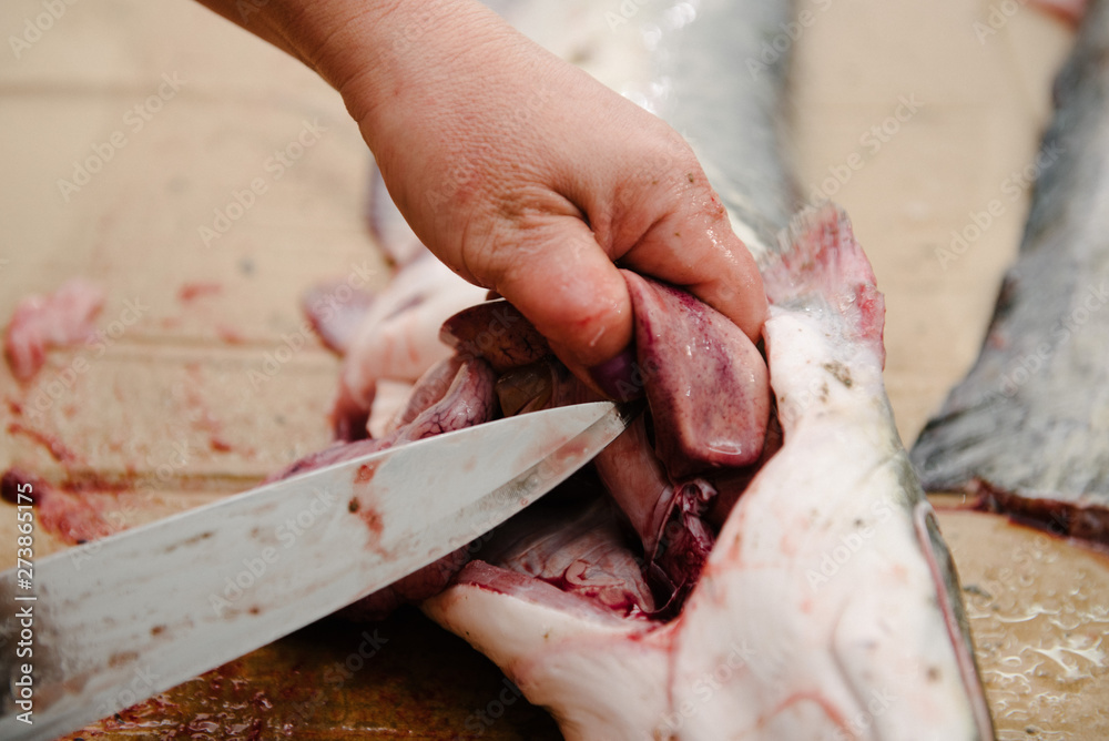 The cook cuts a large fish on the table with a knife