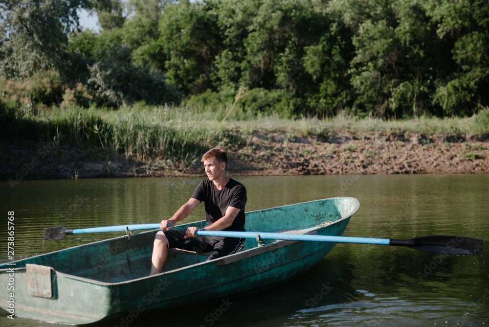 Young man floats on a wooden boat with oars