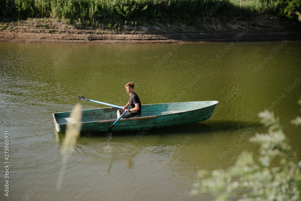 Young man floats on a wooden boat with oars