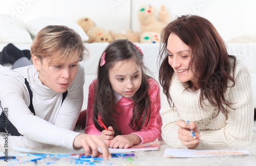 little girl draws with her mother and grandmother