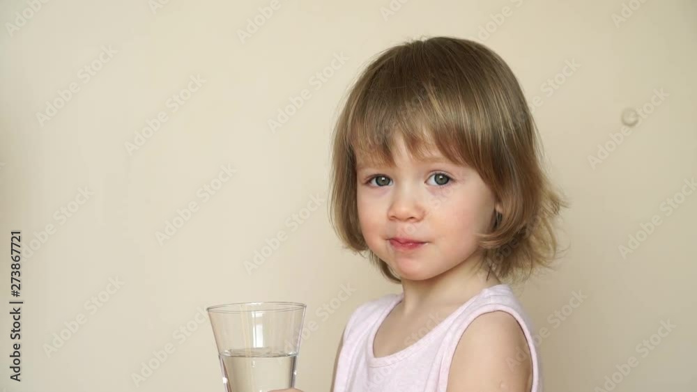 Portrait of little cute child girl holds glass with clean fresh water, drinks and smiles Portrait of little cute child girl holds glass with clean fresh water, drinks and smiles