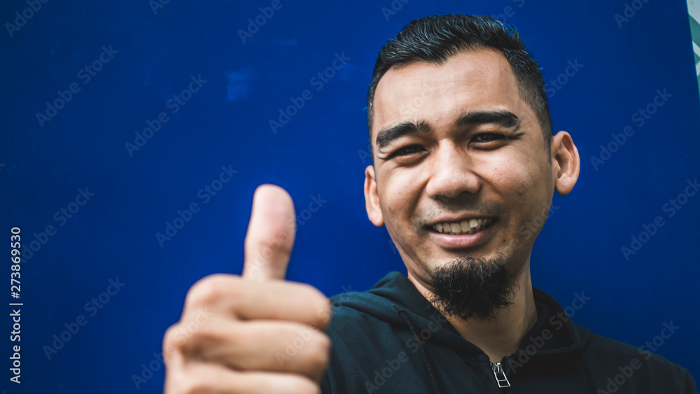 Closeup shot of happy young man showing thumb up in blue background Closeup shot of happy young man showing thumb up in blue background