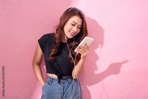 Fashion pretty cool smiling girl, relaxing, listening to music with headphones on a pink background.