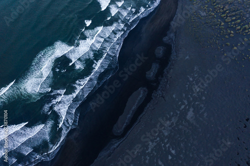 Aerial shot of black stone beach with waves.