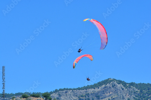 Paragliding. Two paragliders on a blue sky and mountains background. Copy space.
