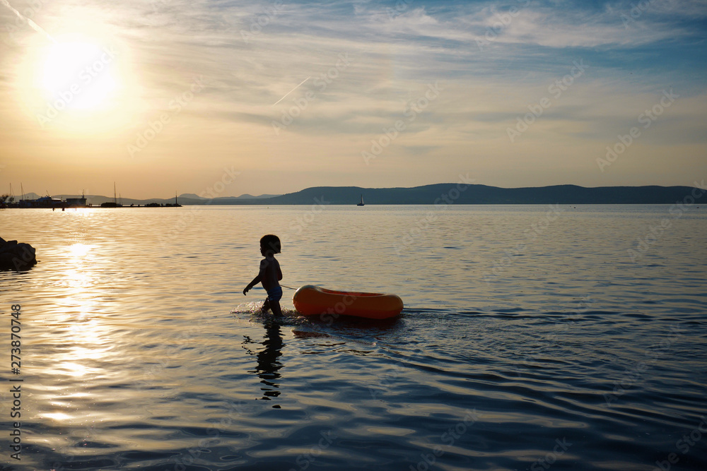 Cute small boy playing with an inflatable boat in Lake Balaton, Hungary
