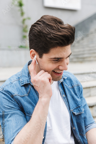 Happy young amazing man businessman posing outdoors outside listening music with earphones.