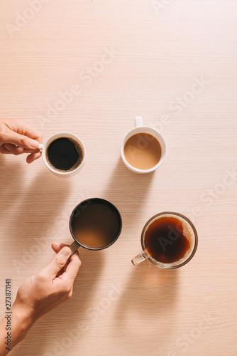 Hands holding cups of coffee on wood background