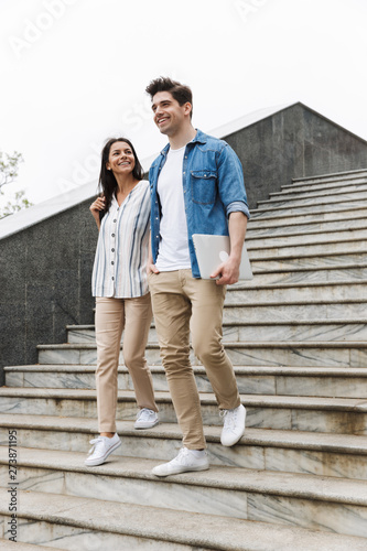 Image of cheerful couple smiling and talking while strolling down stairs outdoors © Drobot Dean