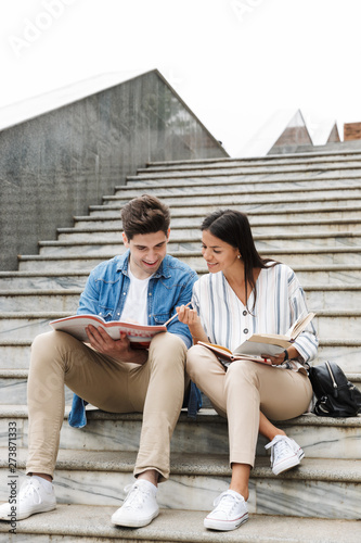 Amazing loving couple students colleagues outdoors outside on steps reading book writing notes studying.