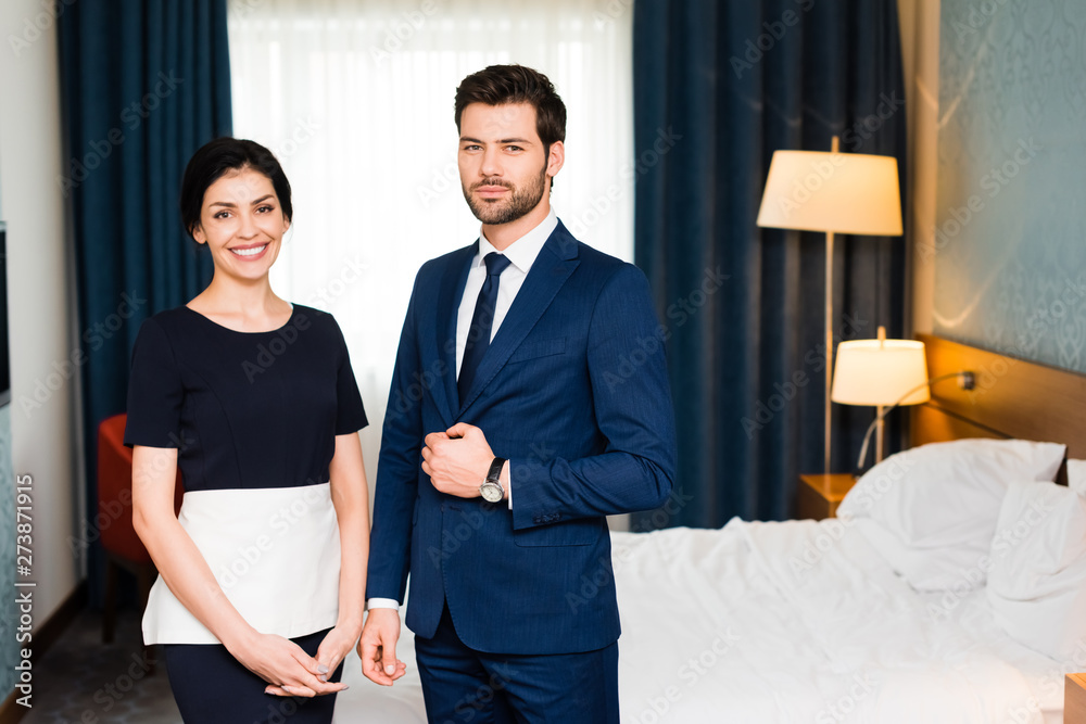 Fototapeta premium happy housemaid smiling near handsome receptionist touching suit