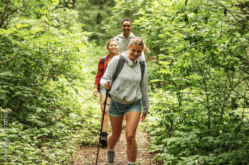 Group of friends hiking in nature.They walking trough forest and meadows.Blond hair female are in focus.
