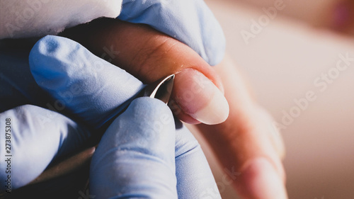 Manicurist master is making manicure for client woman in beauty salon. She is cutting cuticle with professional nail tongs, hands in gloves closeup.