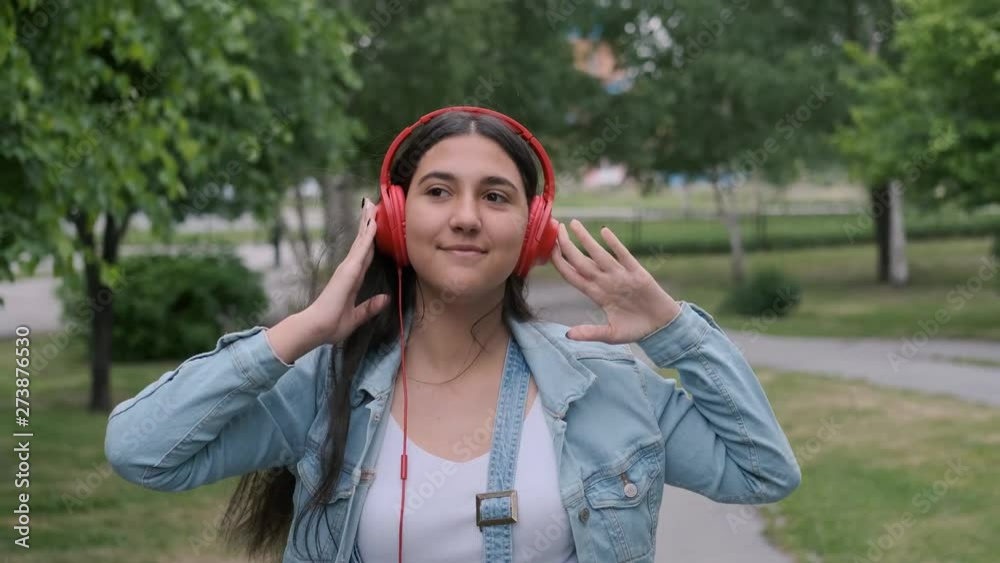 Cheerful beautiful girl in red headphones goes to skip and listens to music Cheerful beautiful girl in red headphones goes to skip and listens to music