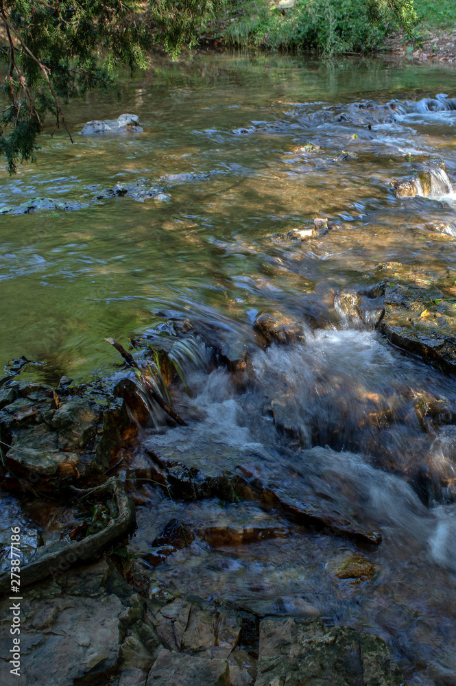 Fototapeta premium After heavy rains this little creek in southwest Missouri make a pretty scene with a little waterfall. The photographer captured a bokeh effect and creamy flowing waters.