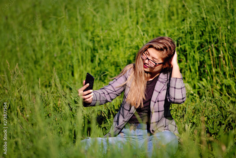 Young beautiful asian girl makes selfie in the grass in summer Young beautiful asian girl makes selfie in the grass in summer