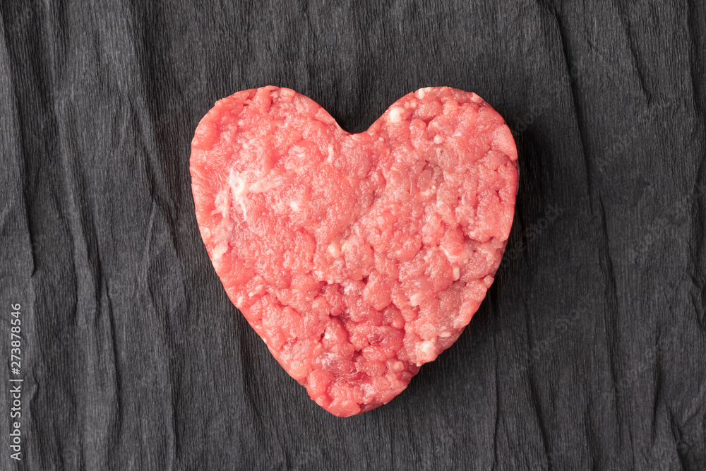 Uncooked ground beef patty on a background of crumpled black paper Uncooked ground beef patty on a background of crumpled black paper