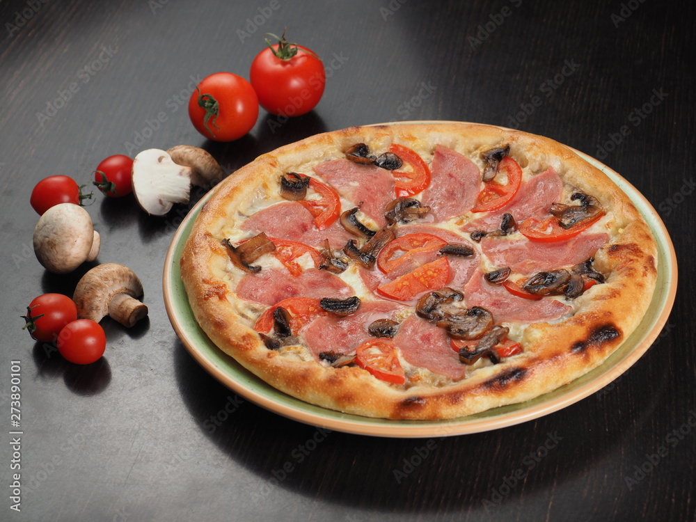Pizza with ham, tomatoes and mushrooms in a plate