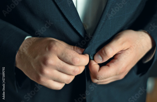Close up of a man in suit tying a button on the jacket