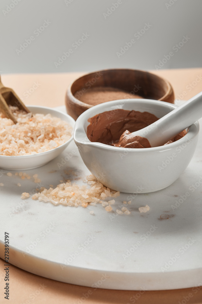 selective focus of clay and sea salt in bowls on marble surface isolated on grey selective focus of clay and sea salt in bowls on marble surface isolated on grey