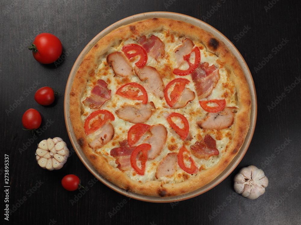 Pizza with ham, chicken, tomatoes and cheese on a plate