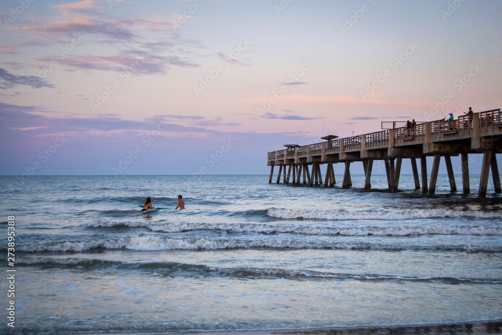 Naklejka premium People surfing by pier in the sunset