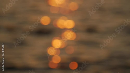 Beautiful golden colors of sunset, small waves with glossy reflexions. Out of focus, sunbeam reflection on calm water surface in evening, golden hour. Focus pulling from blur.