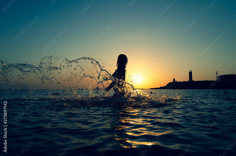 Silhouette of young girl in the water that splashing their hair against sunset