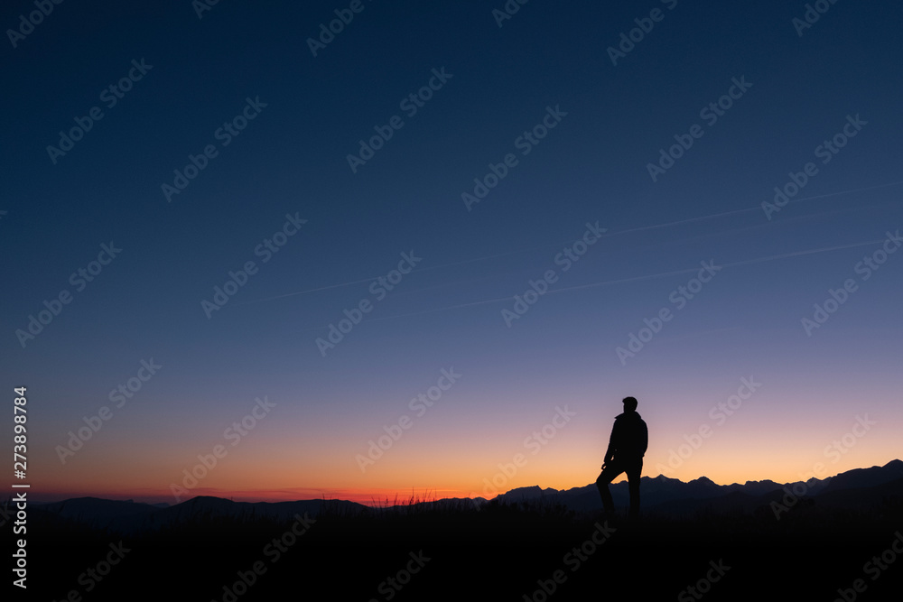 A man looks at the sun rising from the top of a mountain