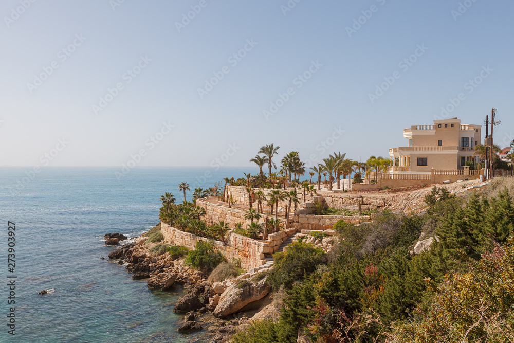 Luxurious house with palms on the steep coast of Mediterranean sea. Cyprus, sunny summer day