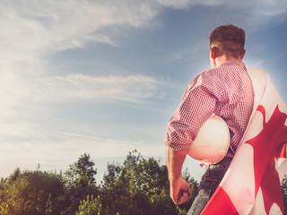 Attractive engineer, holding an Canadian Flag in the park against the backdrop of green trees and the setting sun, looking into the distance. Close-up. Concept of labor and employment