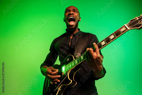 Photography Young african-american musician playing the guitar like a rockstar on gradient green-yellow background