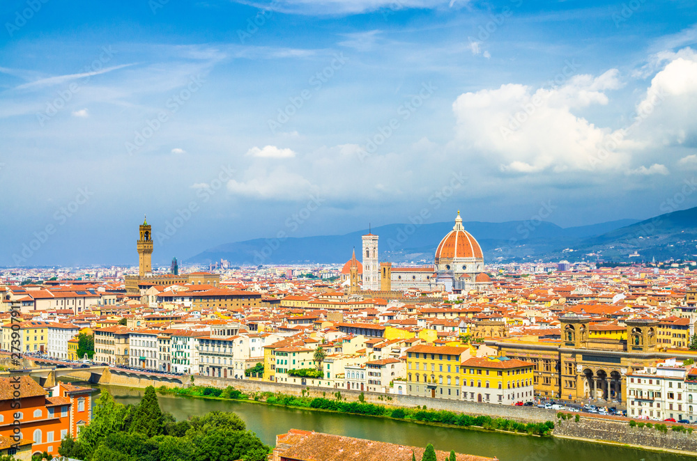 Top aerial panoramic view of Florence city with Duomo Cattedrale di Santa Maria del Fiore cathedral, buildings houses with orange red tiled roofs and Arno river, blue sky white clouds, Tuscany, Italy