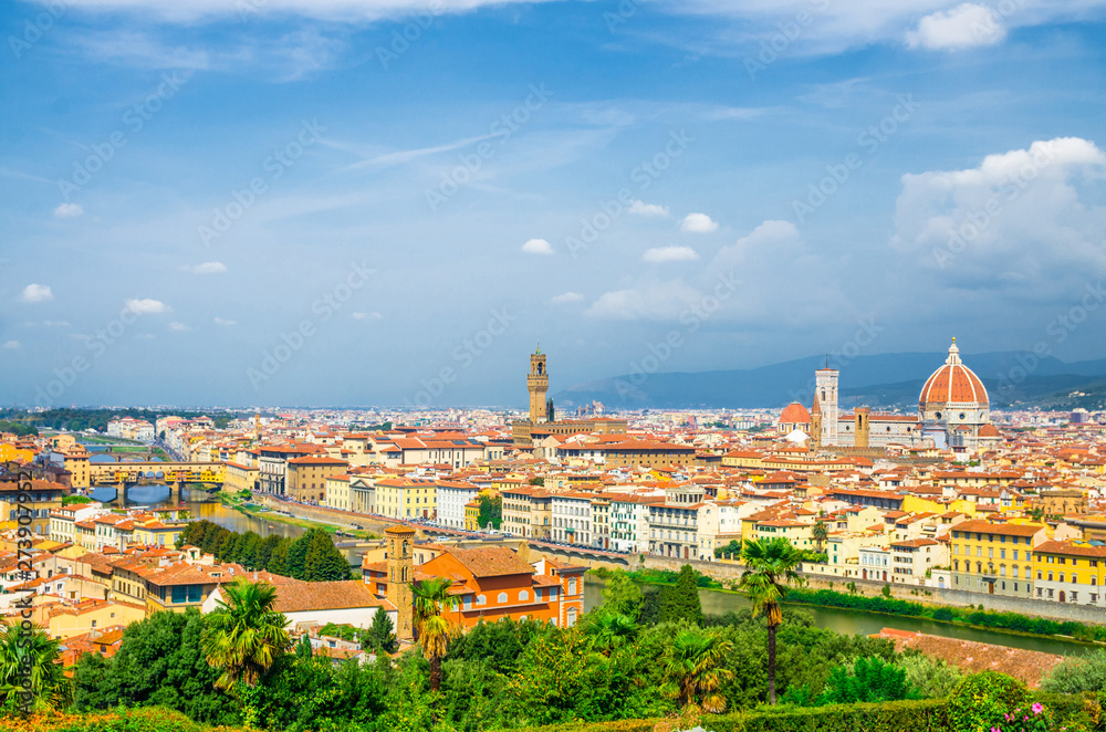 Top aerial panoramic view of Florence city with Duomo Santa Maria del Fiore cathedral, Ponte Vecchio bridge, buildings with orange red tiled roofs, Arno river, blue sky white clouds, Tuscany, Italy
