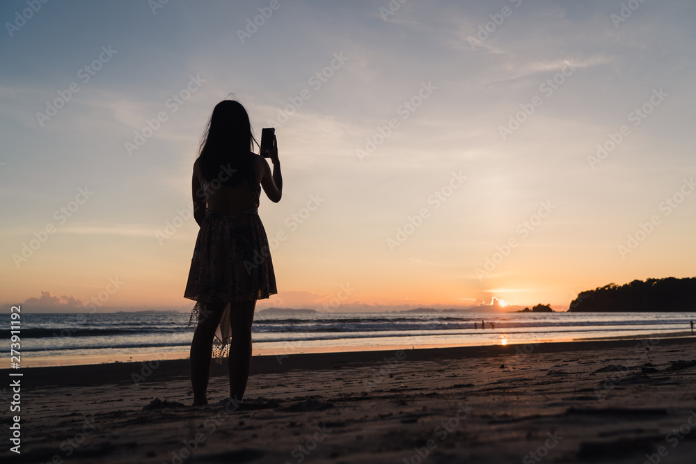 Fototapeta premium Young Asian woman watching sunset near beach, beautiful female happy relax enjoy moment when sunset in evening. Lifestyle woman travel on beach concept.