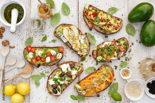 Assorted open faced sandwiches, Open avocado sandwiches made of slices of sourdough bread with various toppings on a white wooden table, top view