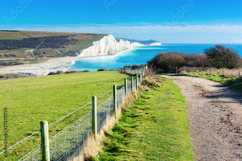 Fototapeta Naklejka Na Ścianę i Meble -  Walk in Cuckmere Haven near Seaford, East Sussex, England. South Downs National park. View of blue sea, cliffs, beach, green fields, selective focus