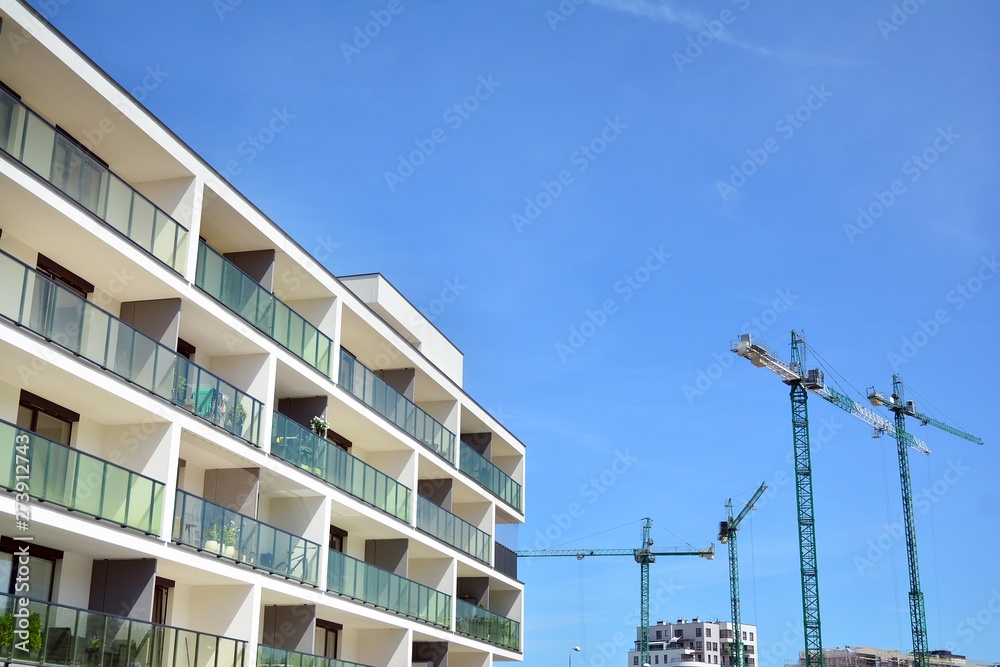 Facade of a modern flat with building cranes in the background