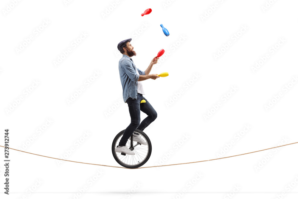 Male juggler with clubs riding a unicycle on a rope - obrazy, fototapety, plakaty 