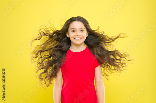 I just let my hair go. Happy child with flowing hair on yellow background. Little kid with cute smile and wavy textured hair. Adorable small girl smiling with long brunette hair