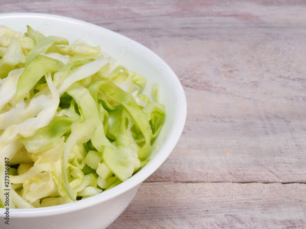 Finely chopped green cabbage in a white bowl on a wooden background with copy space Finely chopped green cabbage in a white bowl on a wooden background with copy space