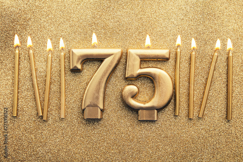 Number 75 gold celebration candle on a glitter background photo