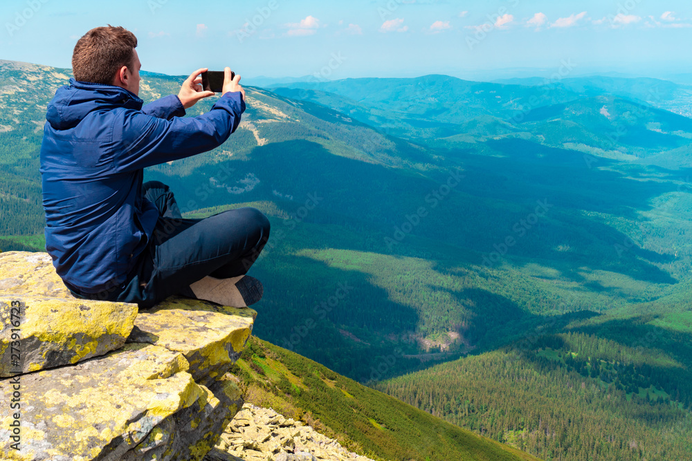 young guy makes a photo on the phone in the mountains