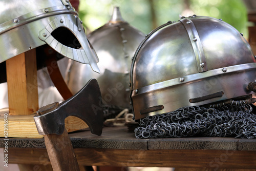 Medieval helmets and battle axe on a wooden table. Armor of middle ages, knightly equipment, armory forge background